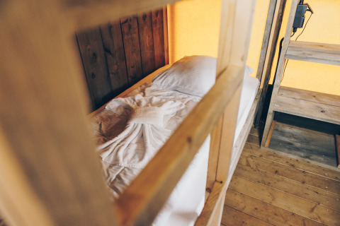 Binnenkant van een safaritent met een eenpersoonsbed, houten meubels en een decoratief gevouwen handdoek op het bed.