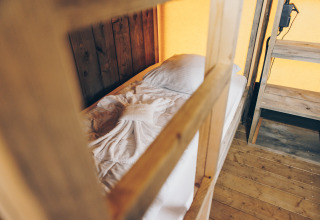 Binnenzicht van een safaritent met een eenpersoonsbed, houten meubels en een sierlijk gevouwen handdoek op het bed.