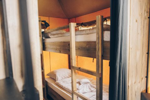 Interieur van een safaritent met houten stapelbedden en warme, sfeervolle canvas wanden.