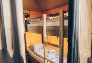 Interieur van een safaritent met houten stapelbedden en warme, sfeervolle canvas wanden.