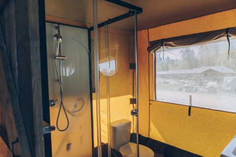 Binnenzicht van een safaritentbadkamer met douche, toilet en raam met zicht op het domein buiten.