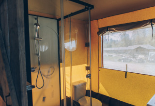 Binnenzicht van een safaritentbadkamer met douche, toilet en raam met zicht op het domein buiten.
