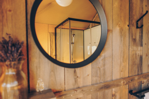 Spiegelbeeld van een douchecabine in een safari tent badkamer met houten wanden en sfeervolle stijl.