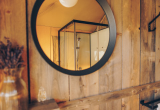 Spiegelbeeld van een douchecabine in een safari tent badkamer met houten wanden en sfeervolle stijl.