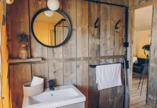 Badkamer met houten wanden, ronde spiegel, wastafel en stijlvolle details in een safaritent.