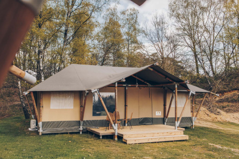 Safaritent Glamfield Lodge met houten veranda en stoelen, omgeven door bomen en groene natuur.