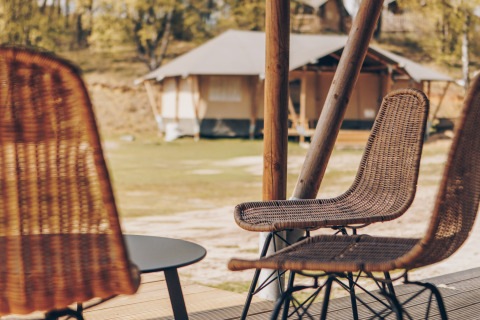 Uitzicht vanaf een terras met rotan stoelen en tafel, met safaritenten in een natuurlijke omgeving.