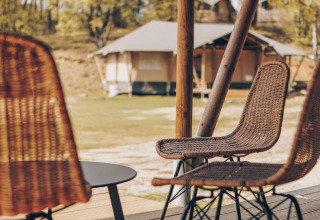 Gezicht vanop een terras met rieten stoelen en tafel voor safaritenten in een groene, open omgeving.