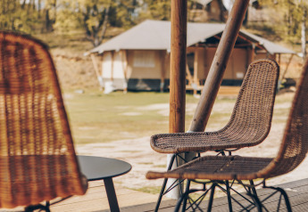 Blick von einer Terrasse mit Korbstühlen und Tisch vor Safarizelten in natürlicher Umgebung im Freien.