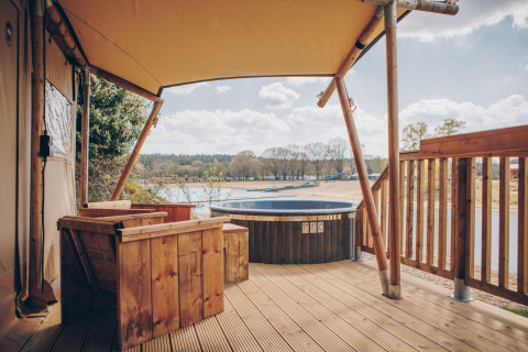 Buitenterras met houten zitplaatsen en bubbelbad bij Glamfield Lodge Premium safaritent met uitzicht op het meer.