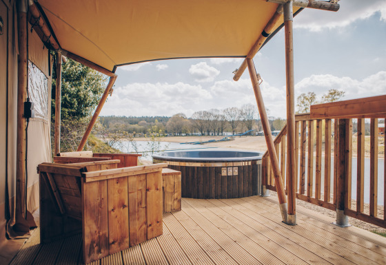 Buitenterras met houten zitplaatsen en bubbelbad bij Glamfield Lodge Premium safaritent met uitzicht op het meer.