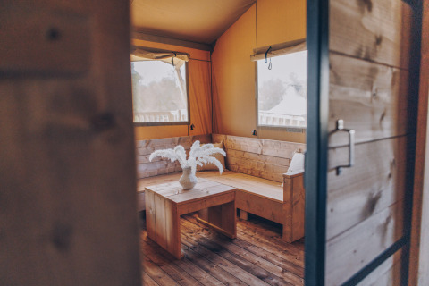 Interieur van safari tent Glamfield Lodge Premium bij Wilsumer Berge, Duitsland, met houten zitbank en tafel.