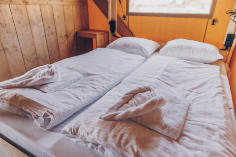 Twee eenpersoonsbedden met witte lakens en handdoeken in een safaritent bij Glamfield Lodge, Wilsumer Berge.