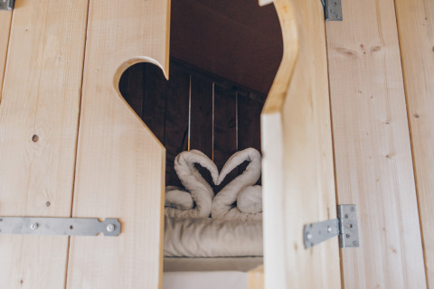 Uitzicht door een houten deur op een bed met handdoekzwanen in Glamfield Lodge Premium, Wilsumer Berge, Duitsland.