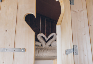 Uitzicht door een houten deur op een bed met handdoekzwanen in Glamfield Lodge Premium, Wilsumer Berge, Duitsland.