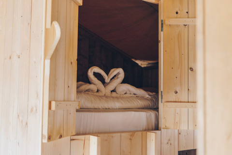 Ingang naar een knus bed in de Glamfield Lodge safaritent, met handdoeken in de vorm van zwanen op het bed.
