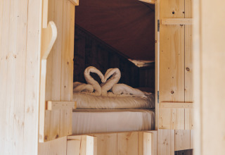Ingang naar een knus bed in de Glamfield Lodge safaritent, met handdoeken in de vorm van zwanen op het bed.