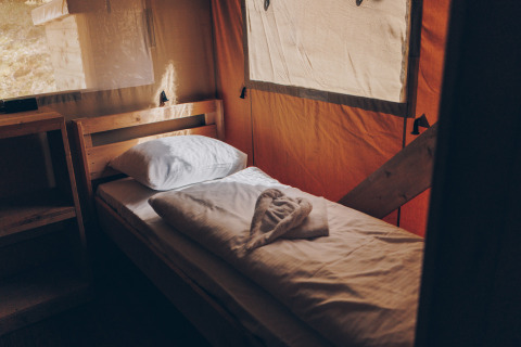 Een eenpersoonsbed met wit beddengoed in een safaritent bij Glamfield Lodge, Wilsumer Berge, Duitsland.