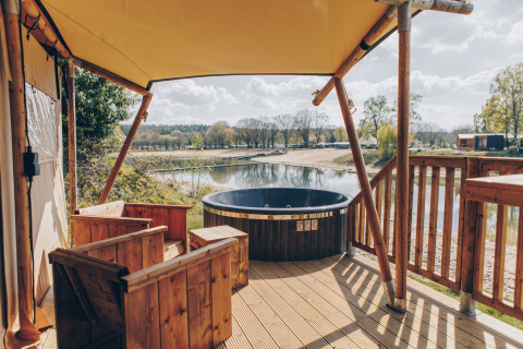 Uitzicht vanaf een safaritent veranda met houten stoelen en hottub bij het meer bij Wilsumer Berge.