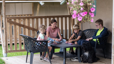 Familie spielt Karten auf der Veranda eines Safarizelts mit Toilette auf Camping de Krabbeplaat in den Niederlanden.