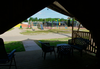 Vue depuis la terrasse d’une tente safari avec sièges extérieurs, aire de jeux et zone d’eau au Camping de Krabbeplaat.