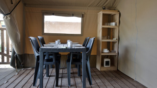 Interior of a safari tent with dining table, black chairs and shelves at Campsite de Krabbeplaat, Netherlands.