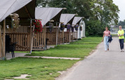 Zwei Personen spazieren an Safarizelten mit Blumenveranda auf Campingplatz de Krabbeplaat, Niederlande.