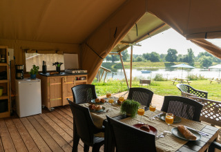 Tenda safari Premium Maaszicht al Campeggio de Boomgaard in Belgio, tavola apparecchiata vista lago.