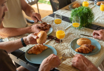 Vier Personen genießen Frühstück mit Croissants, Brötchen und Orangensaft im Safari-Zelt am Campingplatz.