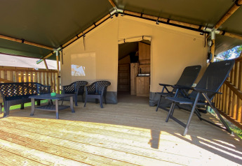 Overdekte veranda met kunststof tuinmeubelen bij safaritent met eigen sanitair op een camping.