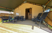 Überdachte Terrasse mit Gartenmöbeln vor einem Safarizelt mit eigenen Sanitäranlagen auf einem Campingplatz.