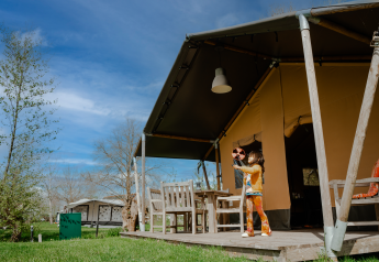 Kind speelt buiten voor safaritent met eigen sanitair op een zonnige dag op de camping.