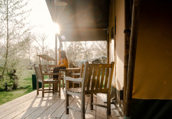Persoon zit op een veranda met houten stoelen bij een safaritent op Camping De Rammelbeek, Nederland.