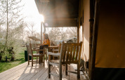 Person sitzt auf einer Terrasse vor einem Safarizelt mit Holzmöbeln auf Campingplatz De Rammelbeek, Niederlande.