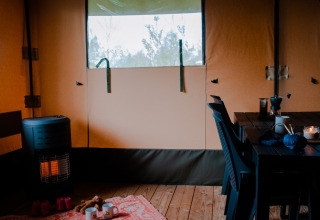 Innenansicht eines Safarizelts mit Ofen, Tisch, Stühlen und Teppich auf Campingplatz De Rammelbeek.