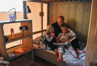 Vater liest zwei Kindern im Schlafanzug eine Geschichte im Safarizelt auf Campingplatz De Rammelbeek vor.