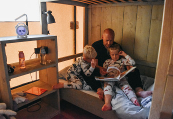 Vater liest zwei Kindern im Schlafanzug eine Geschichte im Safarizelt auf Campingplatz De Rammelbeek vor.