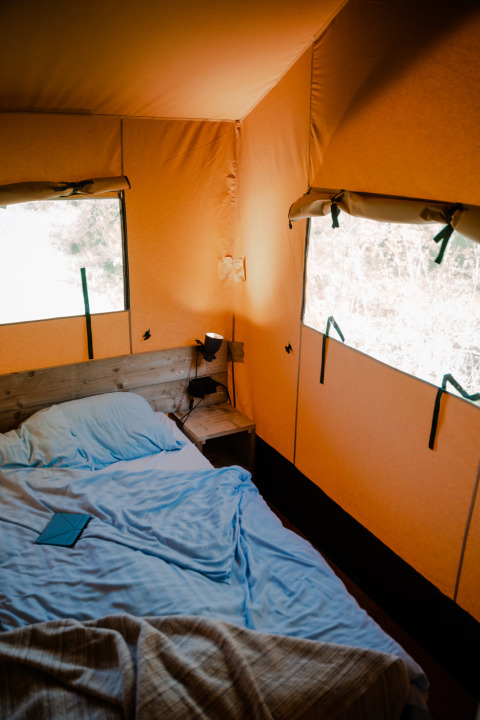 Innenraum eines Safarizelts mit blauem Bett und natürlichen Licht, Sanitäranlagen am Campingplatz Rammelbeek.