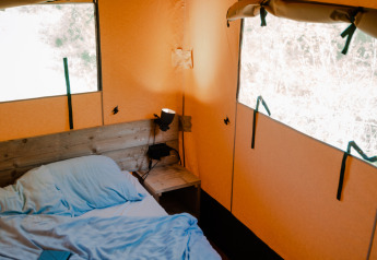 Innenraum eines Safarizelts mit blauem Bett und natürlichen Licht, Sanitäranlagen am Campingplatz Rammelbeek.