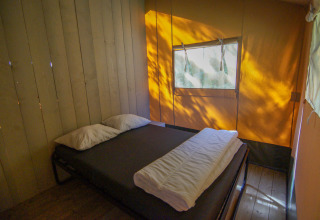 En hyggelig seng i et safari telt på Camping Gorishoek i Holland, sollys falder ind gennem vinduet.