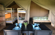 Interno di una tenda safari con letti a castello, letto matrimoniale e tavolo apparecchiato a Camping de Regenboog.