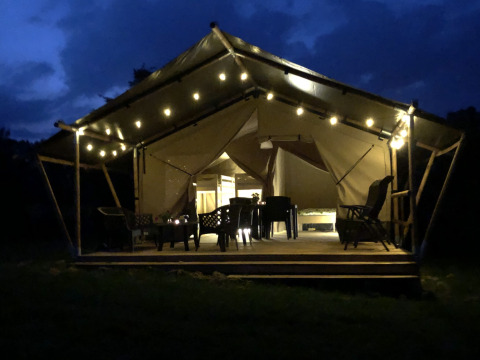 Tenda safari al Camping de Regenboog in Repubblica Ceca, illuminata la sera con luci e sedie all'aperto.