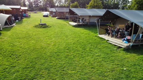 Safari-Zelte und Hütten auf Camping de Regenboog in Tschechien, mit Menschen, die auf der Veranda entspannen.