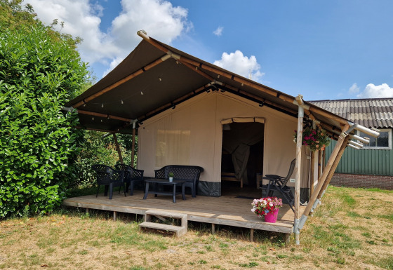 Safari telt med træveranda, plastikstole og blomsterpotte under en blå himmel med skyer.