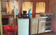 Angolo cucina in tenda safari con frigorifero, macchina del caffè, fornello e scaffale in legno.