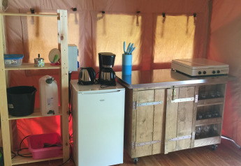 Angolo cucina in tenda safari con frigorifero, macchina del caffè, fornello e scaffale in legno.