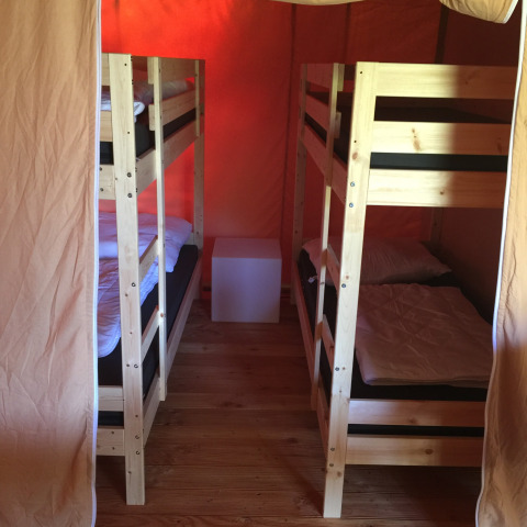 Interieur van een safaritent met twee houten stapelbedden, eenvoudige inrichting en houten vloer.