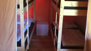 Interieur van een safaritent met twee houten stapelbedden, minimalistische meubels en houten vloer.