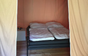 Innenansicht eines Safarizeltes mit Doppelbett, Holzfußboden und hellen Stoffvorhängen.