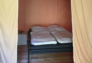 Binnenkant van een safaritent met een tweepersoonsbed, houten vloer en lichte gordijnen.